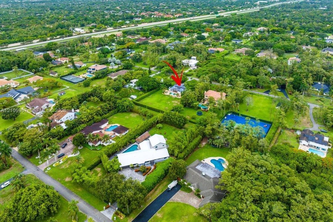 Aerial perspective of a multi-structure property featuring a detached residence, extensive green space, mature landscaping, and mature trees