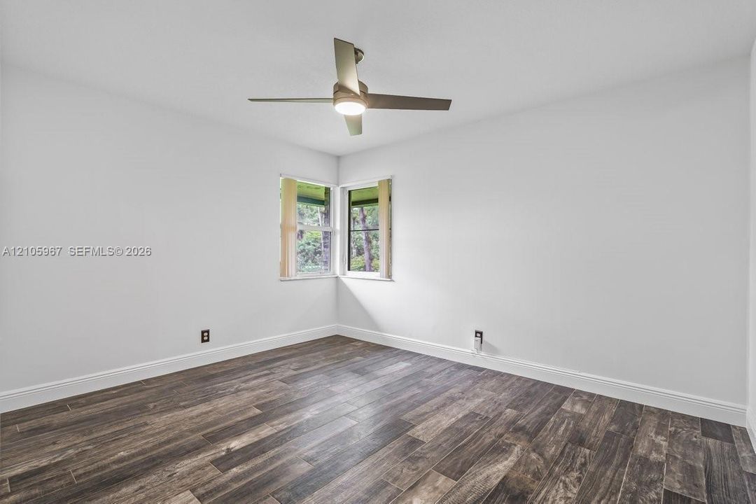 Room featuring wood-finish flooring, white walls, corner windows, and a ceiling-mounted light fixture with fan