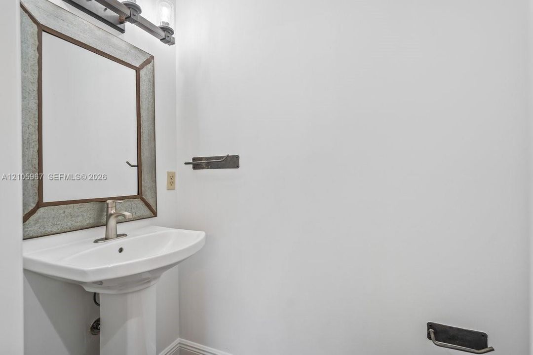 Pedestal sink with a single-handle faucet, metal-framed wall mirror, and industrial-style wall-mounted lighting fixture