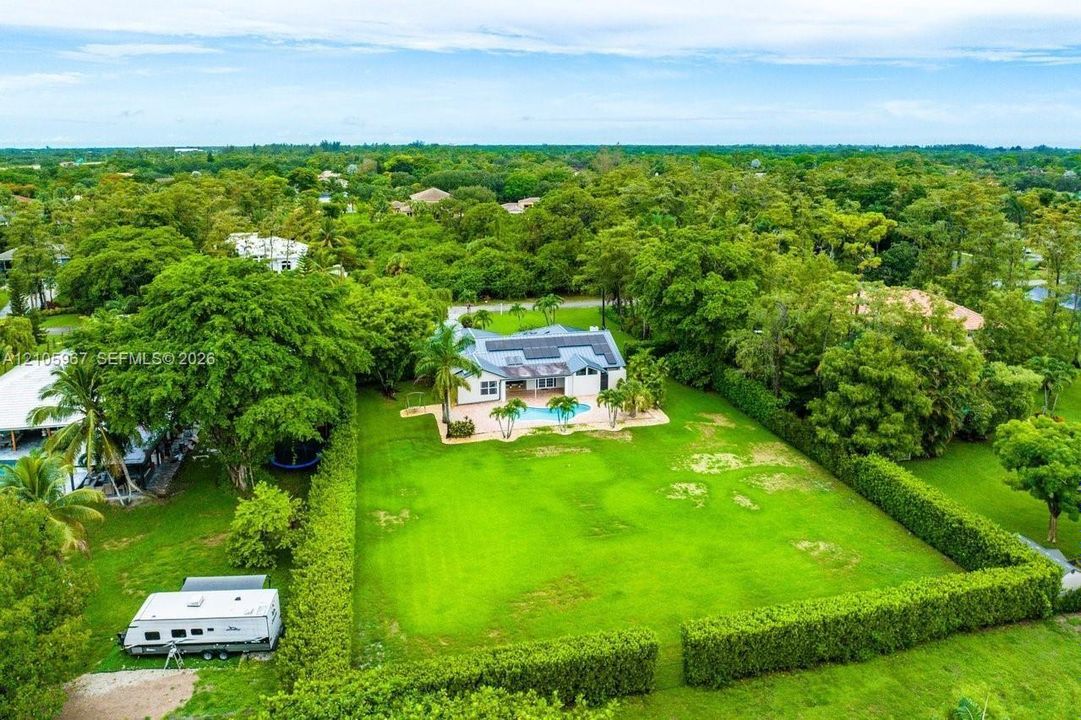 Expansive lot featuring a structured hedge perimeter, swimming pool, and roof-mounted solar panels