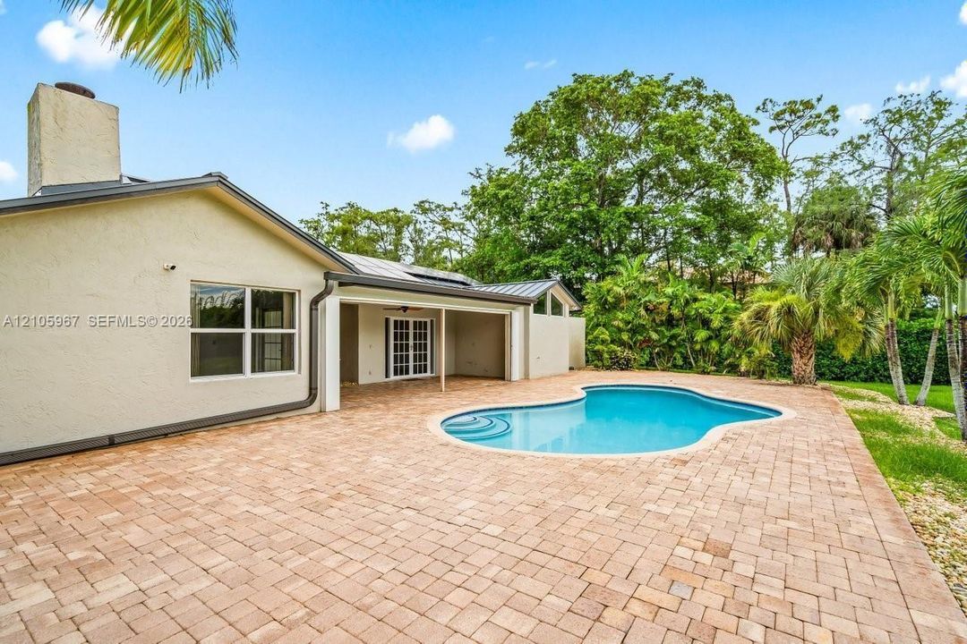 Backyard featuring a paved patio, a freeform swimming pool with integrated steps, a covered lanai, and mature landscape