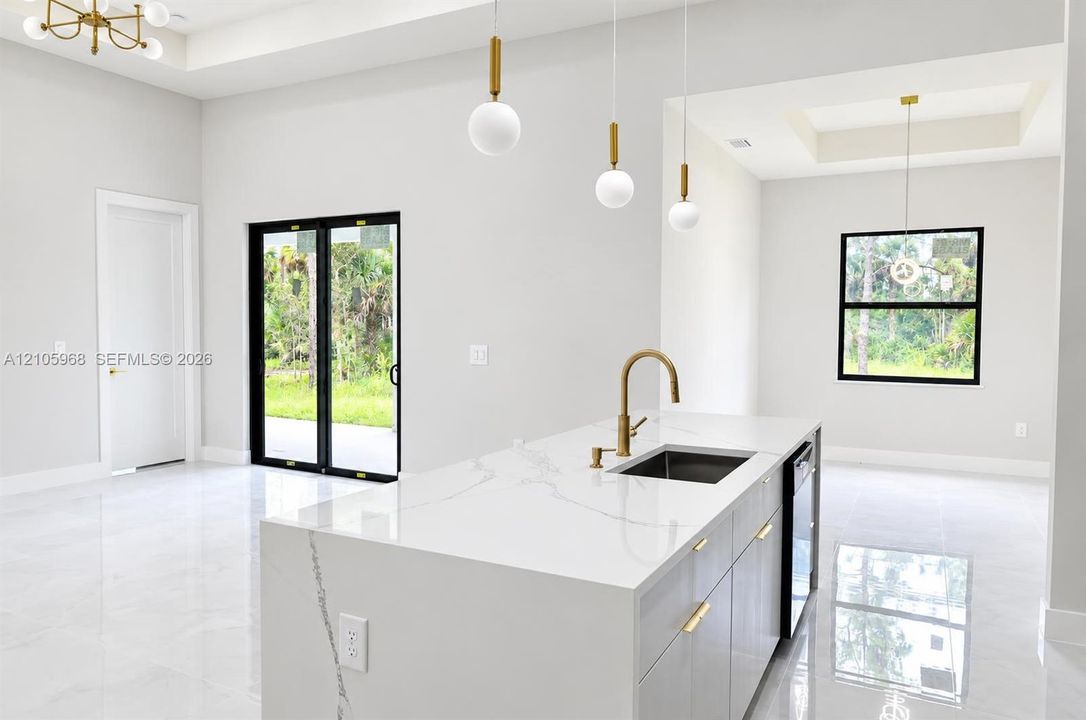 Kitchen island featuring a waterfall-edge countertop, undermount sink with a brass faucet, contemporary pendant lighting, light-tone cabinetry with gold-finish hardware, and large-format tile flooring