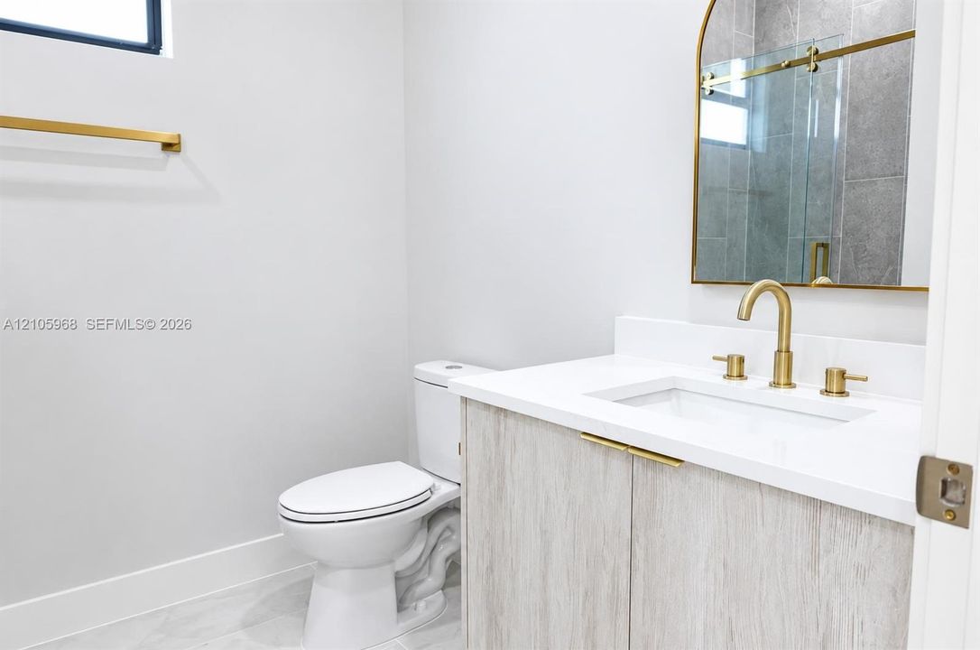 Vanity featuring light wood-finish cabinetry, a white countertop with an integrated rectangular sink, brass hardware, an arched mirror, and a wall-mounted faucet