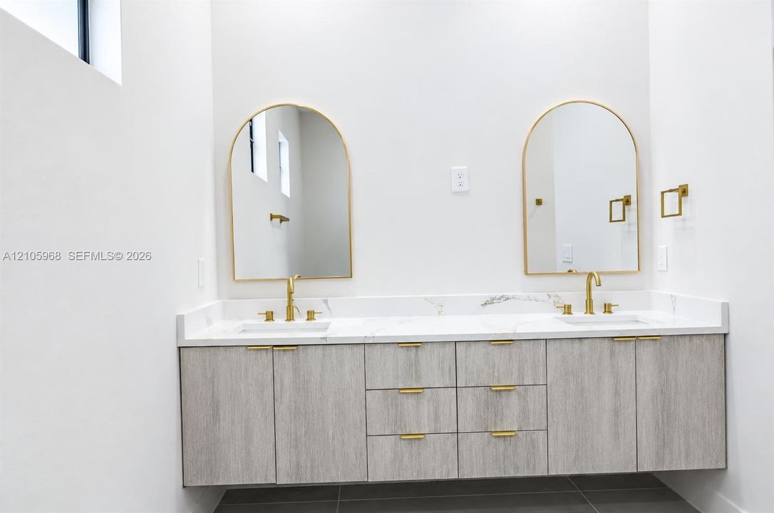 Floating vanity with wood-finish cabinetry, dual undermount sinks, stone-surface countertop, arched mirrors, and brass-tone fixtures