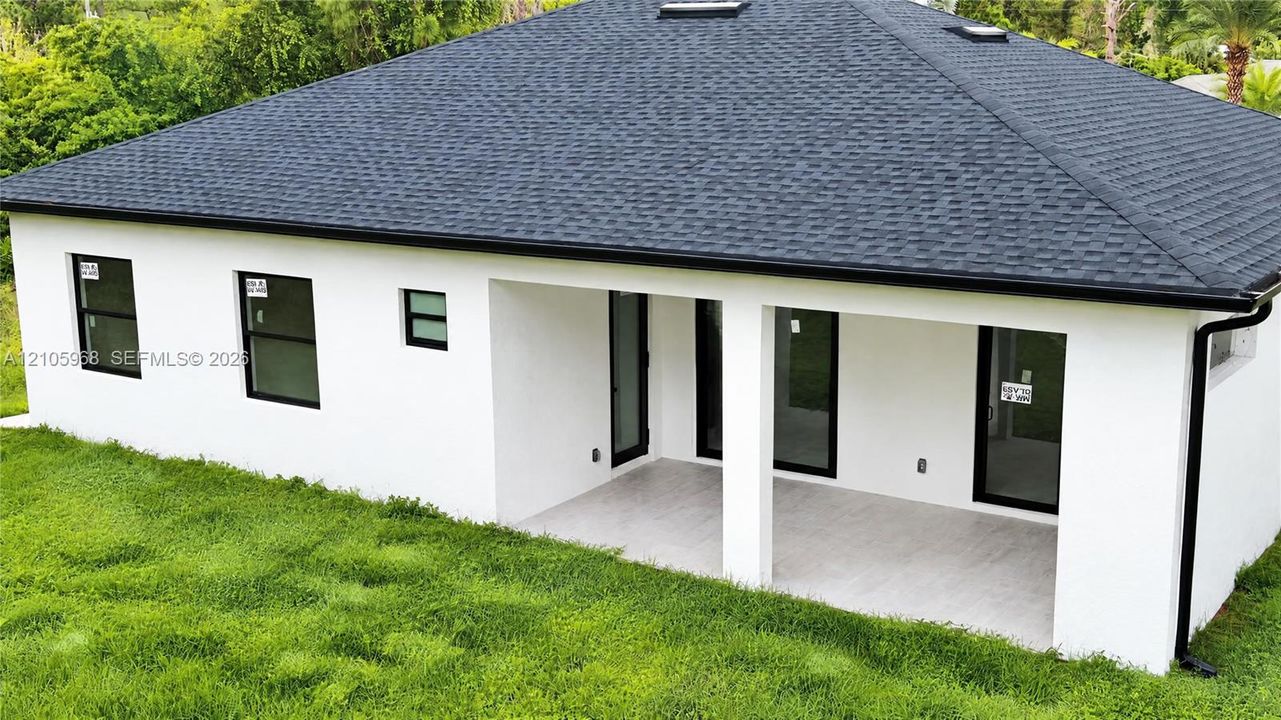 Stucco exterior featuring a covered patio, shingle roof with skylights, and dark-trimmed windows