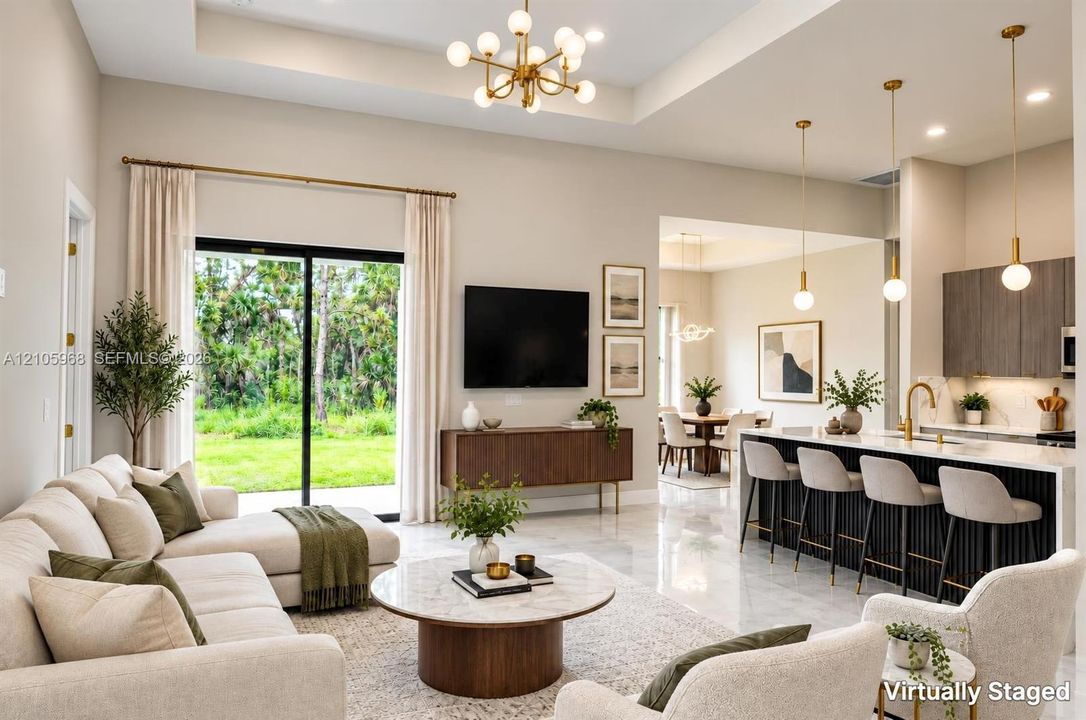 Open-concept living space featuring high tray ceilings, polished tile flooring, a kitchen island with vertical slat detailing, and sliding glass doors