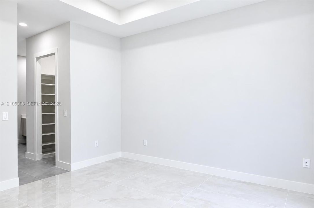 Tray ceiling, recessed lighting, and large-format tile flooring, featuring a walk-in storage area with custom shelving