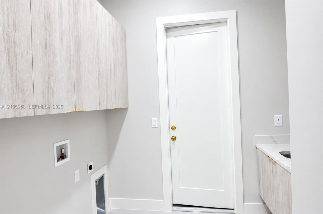 Wall-mounted wood-finish cabinetry, solid-core shaker-style door with brass hardware, stone-surface countertop, and built-in basin