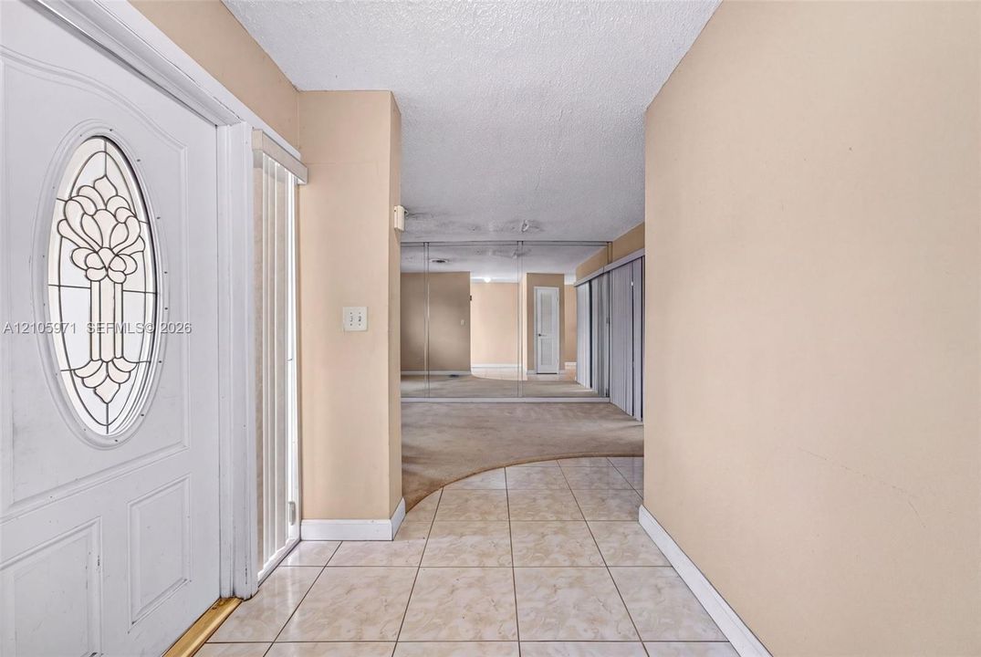Entryway featuring a white door with an oval decorative glass insert, ceramic tile flooring, and wall-to-wall mirrored closet doors