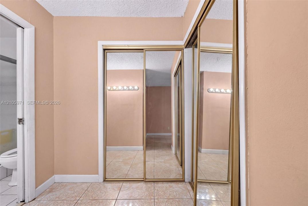 Floor-to-ceiling mirror-paneled sliding closet doors with gold-tone metal framing, ceramic tile flooring, and wall-mounted vanity lighting