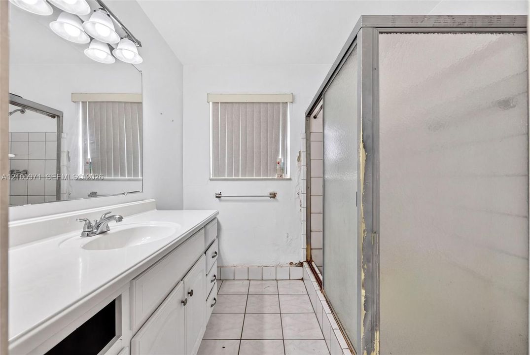 Bathroom featuring a white vanity with an integrated sink, polished chrome faucet, multi-bulb light fixture, tile flooring, and a glass-enclosed shower
