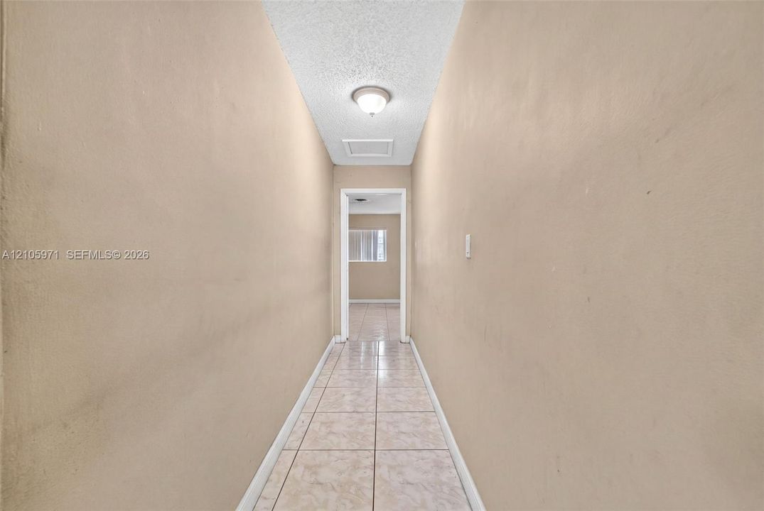 Hallway featuring neutral-toned walls, tile flooring, and a ceiling-mounted light fixture
