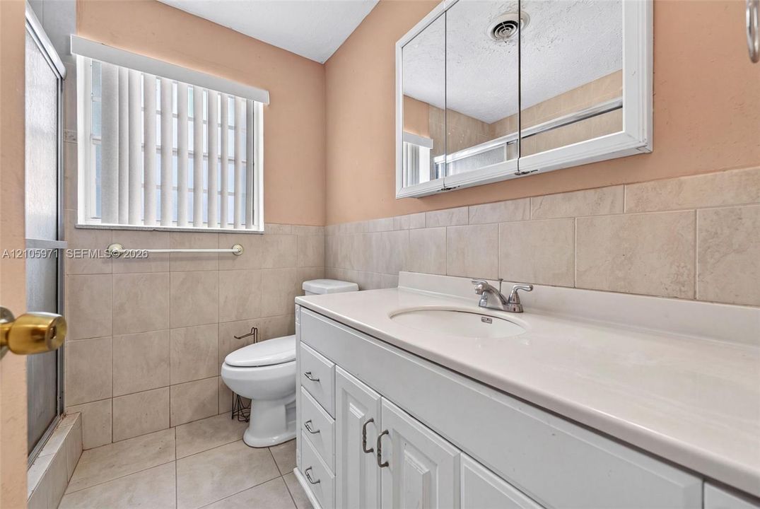 Bathroom featuring a white vanity with an integrated countertop, recessed medicine cabinet, neutral wall tile, and ceramic tile flooring