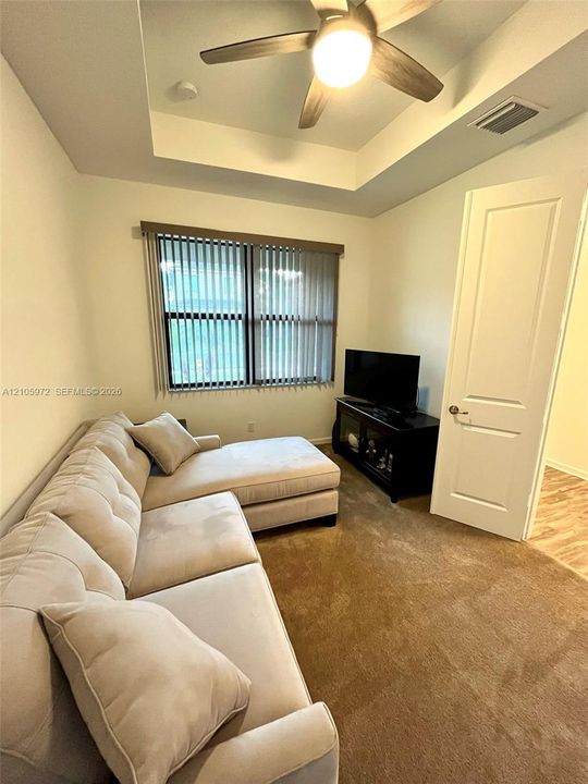 Tray ceiling featuring a central lighted ceiling fan, carpeted flooring, and a single-panel interior door