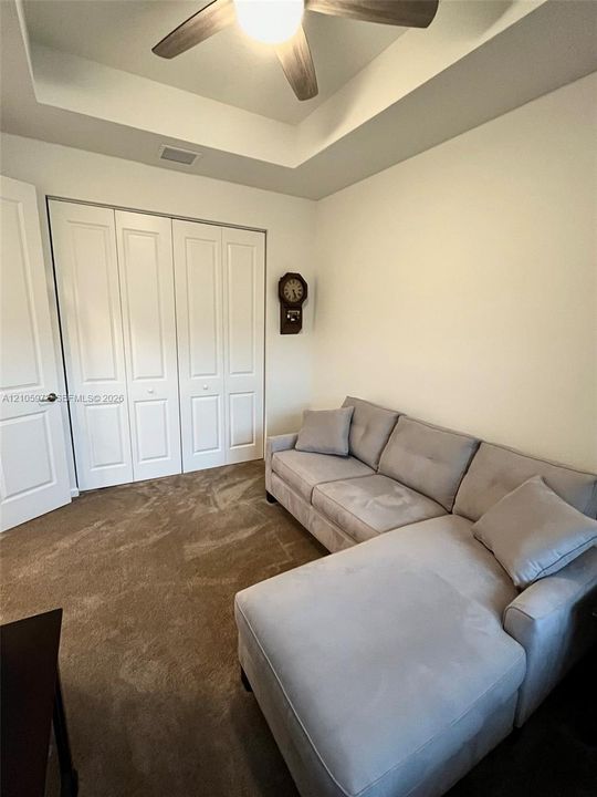 Tray ceiling with a central multi-blade ceiling fan, wall-to-wall carpeted flooring, and white paneled bi-fold closet doors
