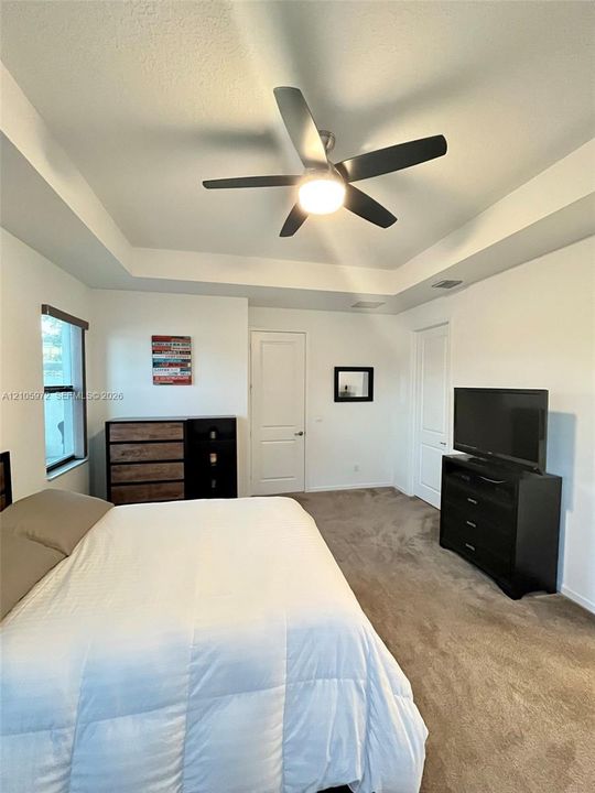 Tray ceiling with a central multi-blade ceiling fan and wall-to-wall carpeting