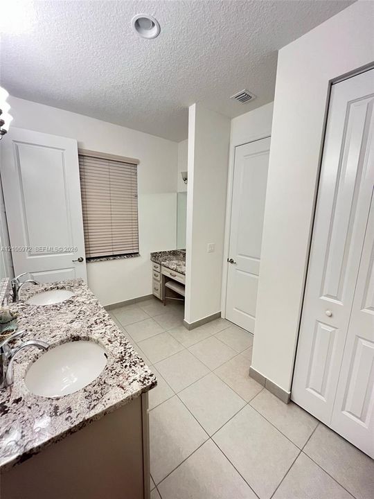 Bathroom featuring a dual-sink vanity with stone-surface countertops, recessed lighting, tile flooring, and a dedicated vanity seating area with integrated cabinetry