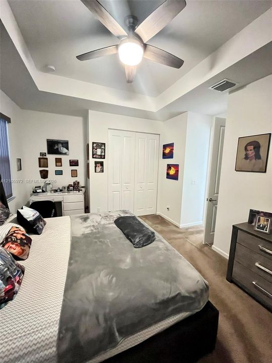 Tray ceiling featuring a central multi-blade ceiling fan with integrated lighting and double-door closet cabinetry