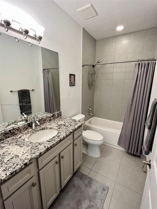 Bathroom featuring light-toned cabinetry, patterned stone-finish countertop, undermount sink, large wall mirror, and tub-shower combination with tile surround