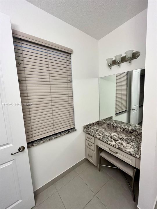 Built-in vanity featuring a stone countertop, three-drawer cabinetry, large wall-mounted mirror, and three-bulb vanity lighting fixture