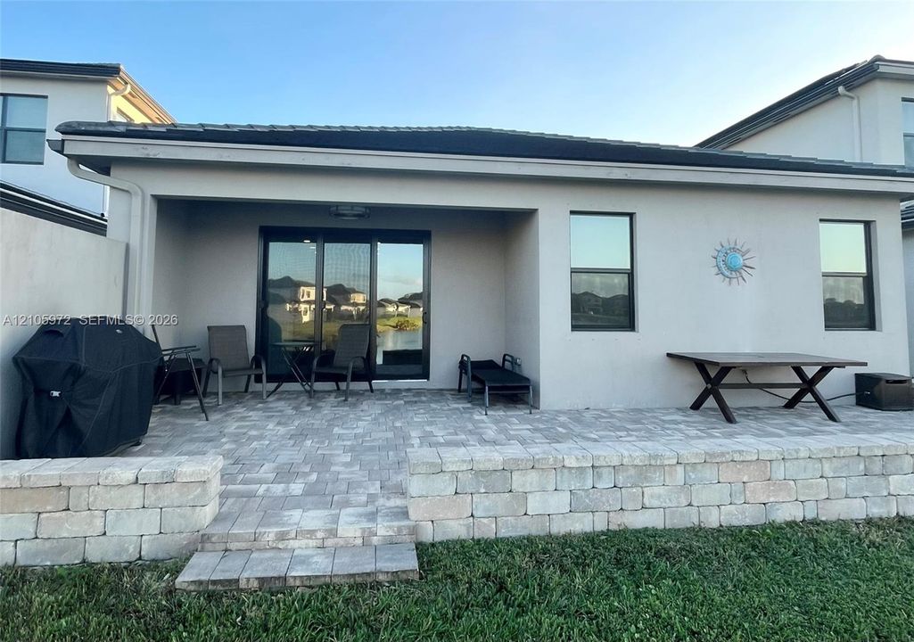 Covered concrete patio featuring pavers, a decorative block retaining wall, and sliding glass door access