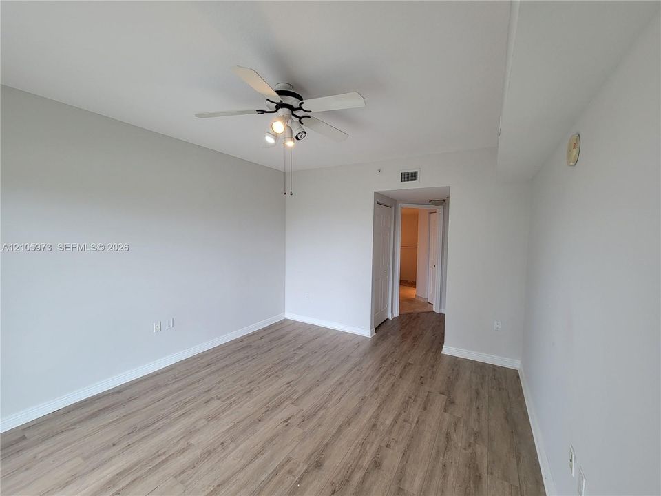 Neutral interior space featuring wood-finish flooring, a ceiling fan with integrated lighting, and a six-panel interior door