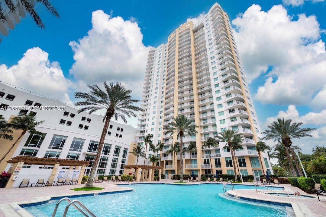 High-rise residential building featuring expansive private balconies, a multi-level swimming pool, integrated spa, and shaded pergola structures