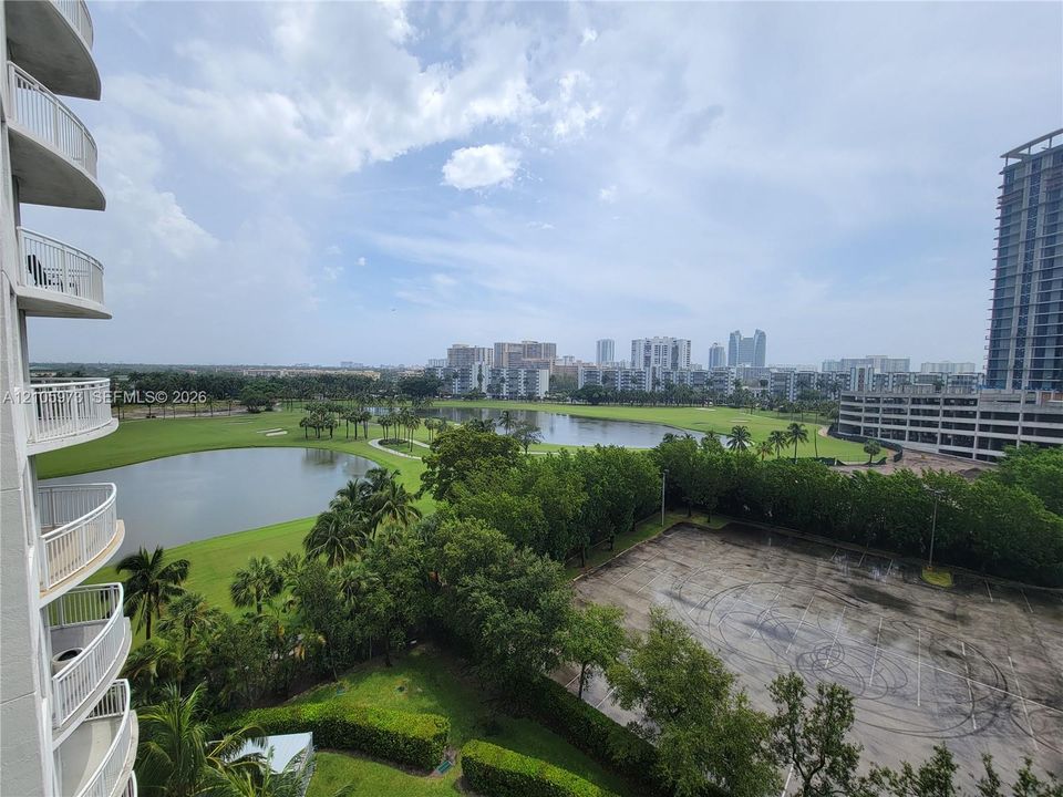 High-rise exterior with stacked balconies, overlooking a lake, manicured green space, and urban landscape