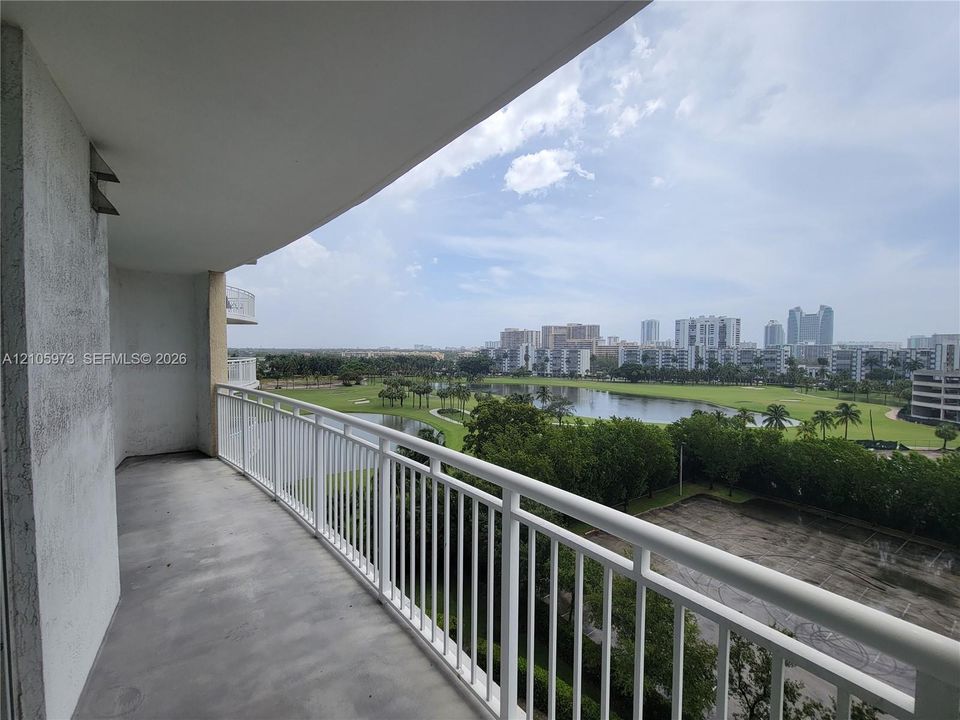Covered balcony featuring concrete flooring and a white metal railing, overlooking a landscaped water feature and surrounding cityscape
