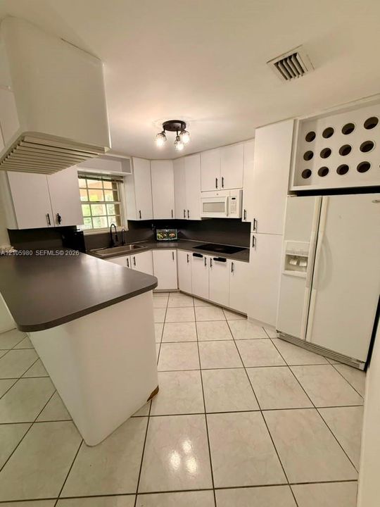 Kitchen featuring white cabinetry, integrated wine storage, contrasting dark countertops, a peninsula, and tile flooring