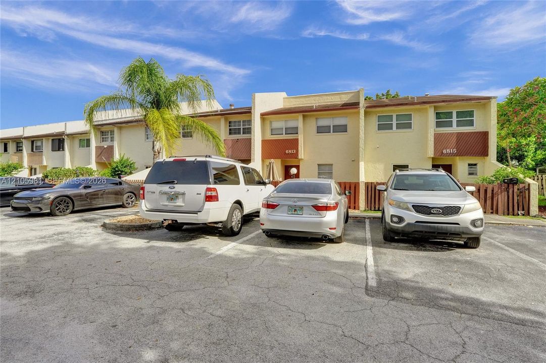 Multi-unit exterior featuring a painted stucco finish, horizontal paneling accents, individual private entries, and paved surface parking