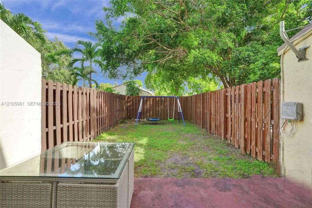 Fenced-in backyard featuring a grass lawn and mature trees