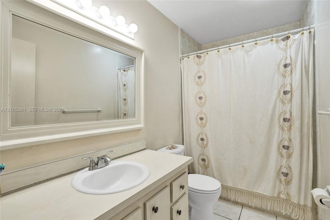 Bathroom featuring a vanity with integrated sink, chrome-finish faucet, framed wall-mounted mirror, overhead multi-bulb lighting, and a tiled shower surround