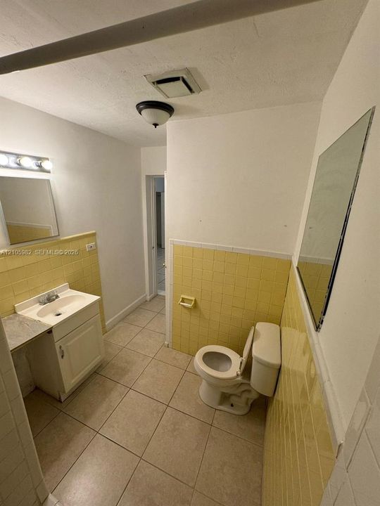 Bathroom featuring ceramic tile flooring, yellow ceramic wall tiling, vanity with a laminate countertop, wall-mounted mirror, and ceiling-mounted light fixture