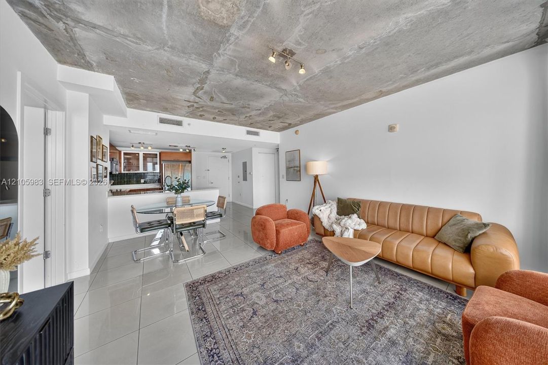 Open-concept living space featuring an exposed concrete ceiling, polished tile flooring, and a kitchen island with built-in cabinetry