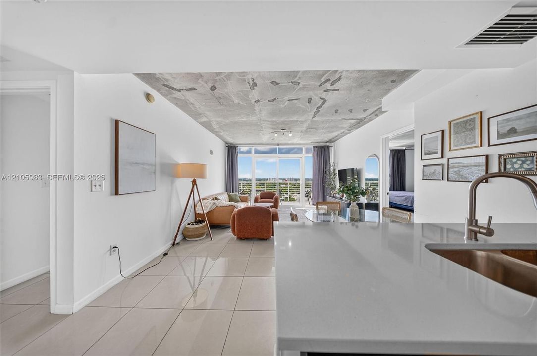 Open-concept interior featuring a high-contrast exposed concrete ceiling, polished tile flooring, and large-format sliding glass doors