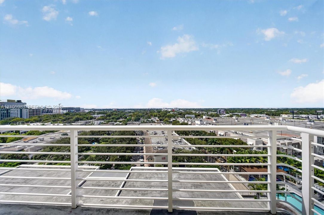 Private balcony with horizontal metal railing, concrete flooring, and extensive cityscape horizon