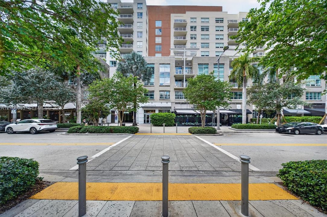 Multi-story mixed-use building featuring a glass and masonry facade, private balconies, and ground-level storefronts surrounded by mature landscaping