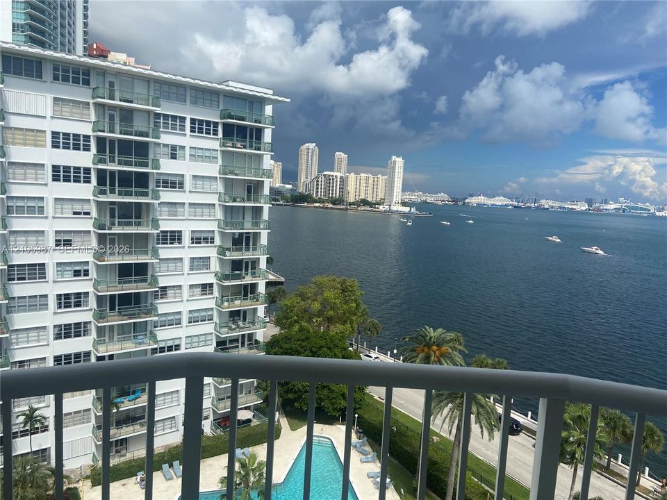 Balcony with metal railing overlooking a swimming pool, waterfront, and cityscape