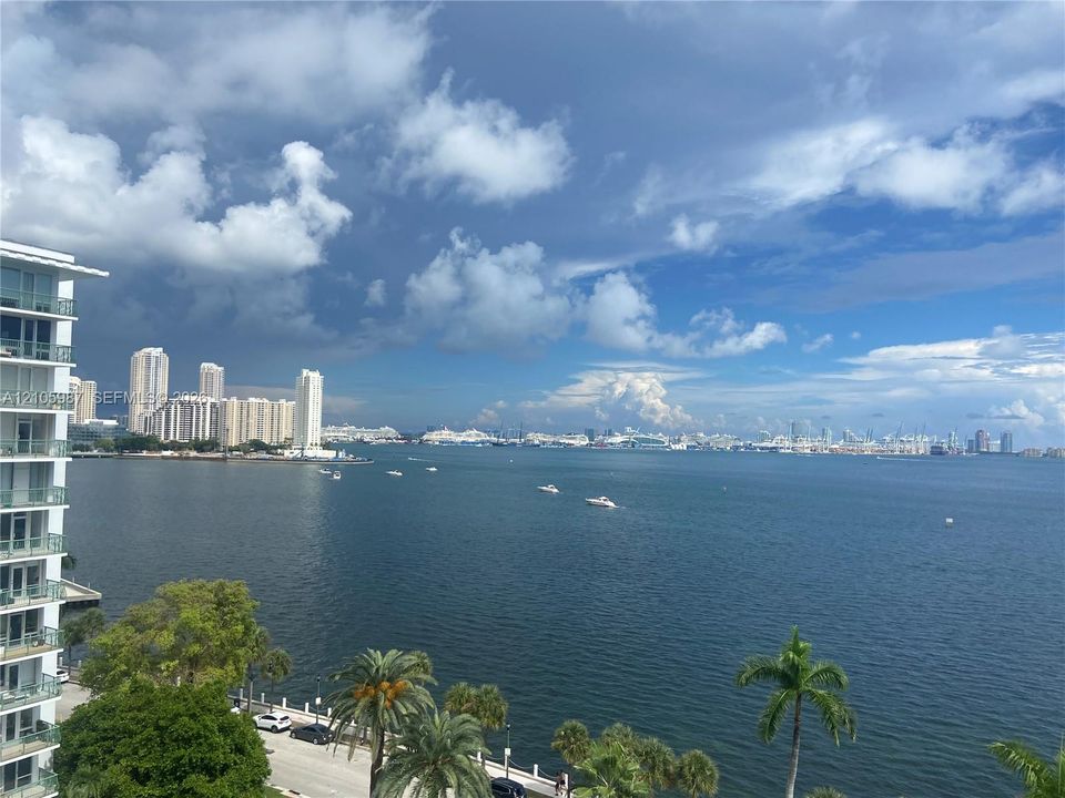 High-rise structure featuring glass-railed balconies and panoramic coastal scenery of the bay, city skyline, and mature palm trees