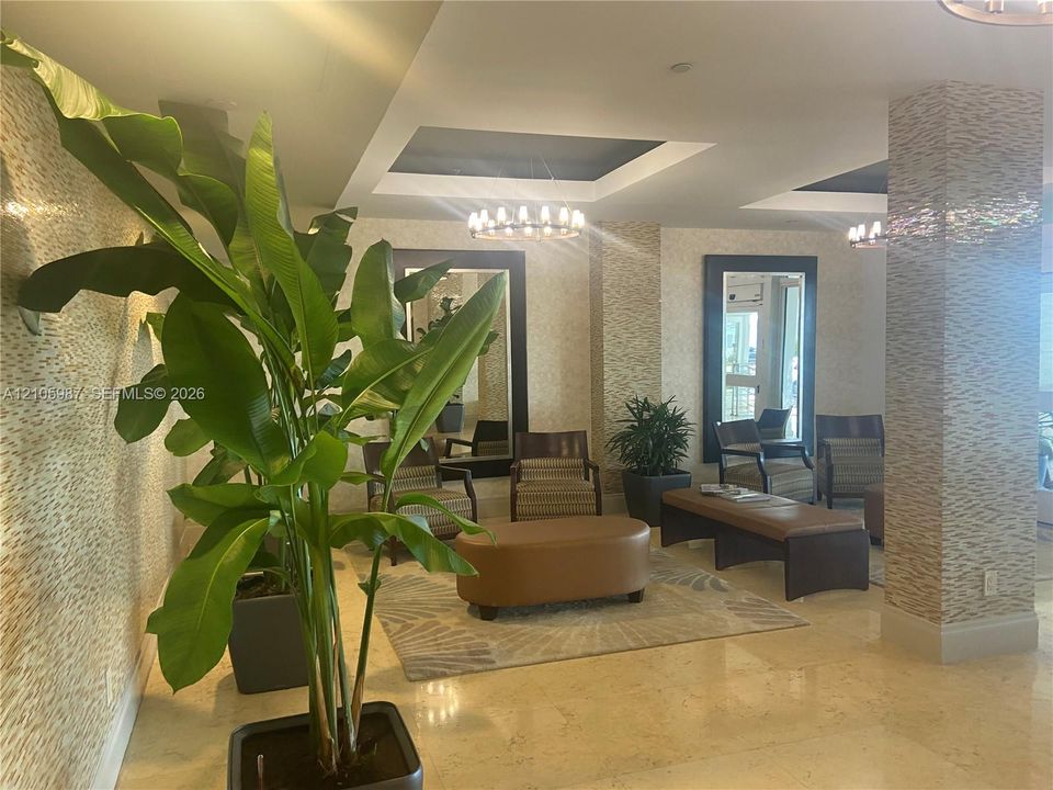 Reception area featuring textured wall coverings, stone-tile flooring, recessed tray ceilings, and dual decorative chandeliers