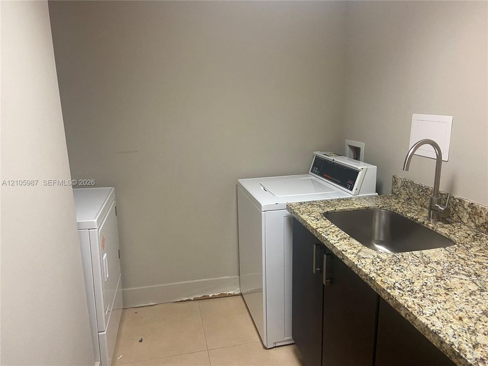 Laundry room featuring a stone countertop, under-mount stainless steel sink with a high-arc faucet, dark cabinetry, and tile flooring
