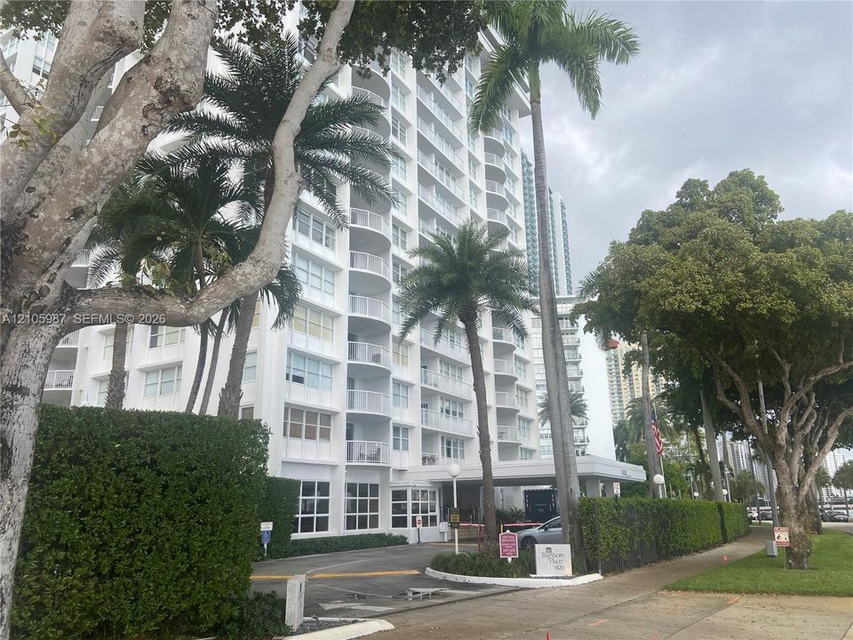 High-rise building exterior featuring tiered balconies, a covered entryway, and mature palm tree landscaping