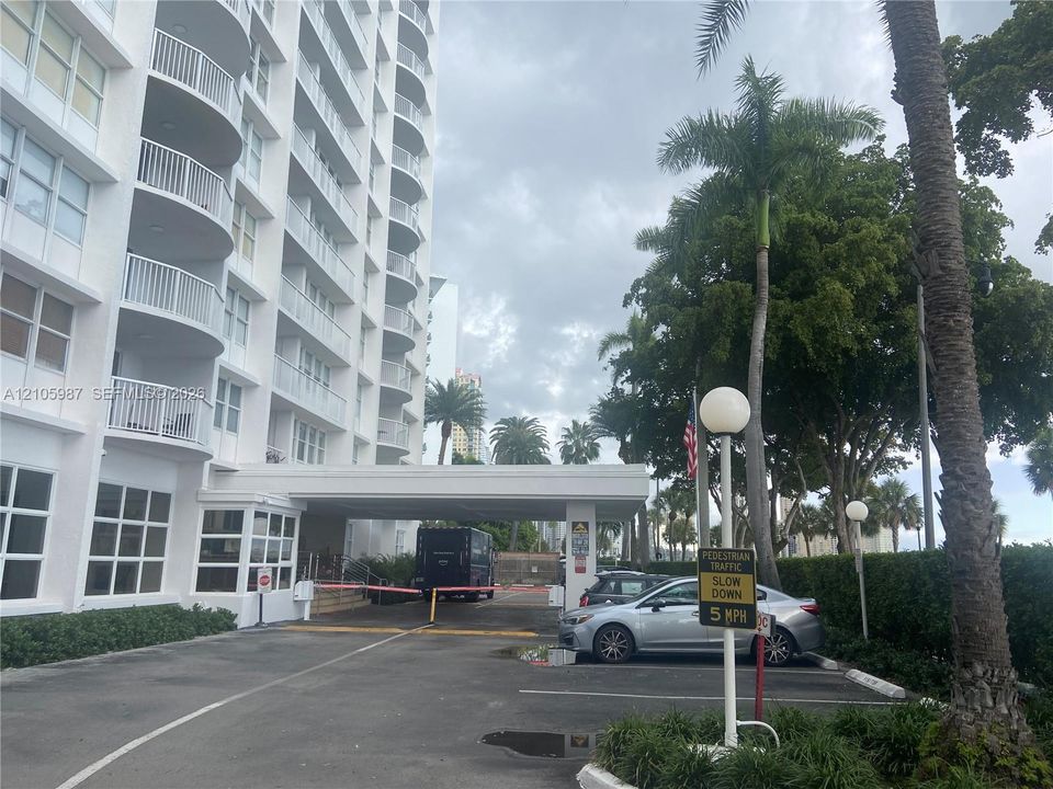 High-rise residential exterior featuring a covered porte-cochère, multi-level balconies, and manicured tropical landscaping