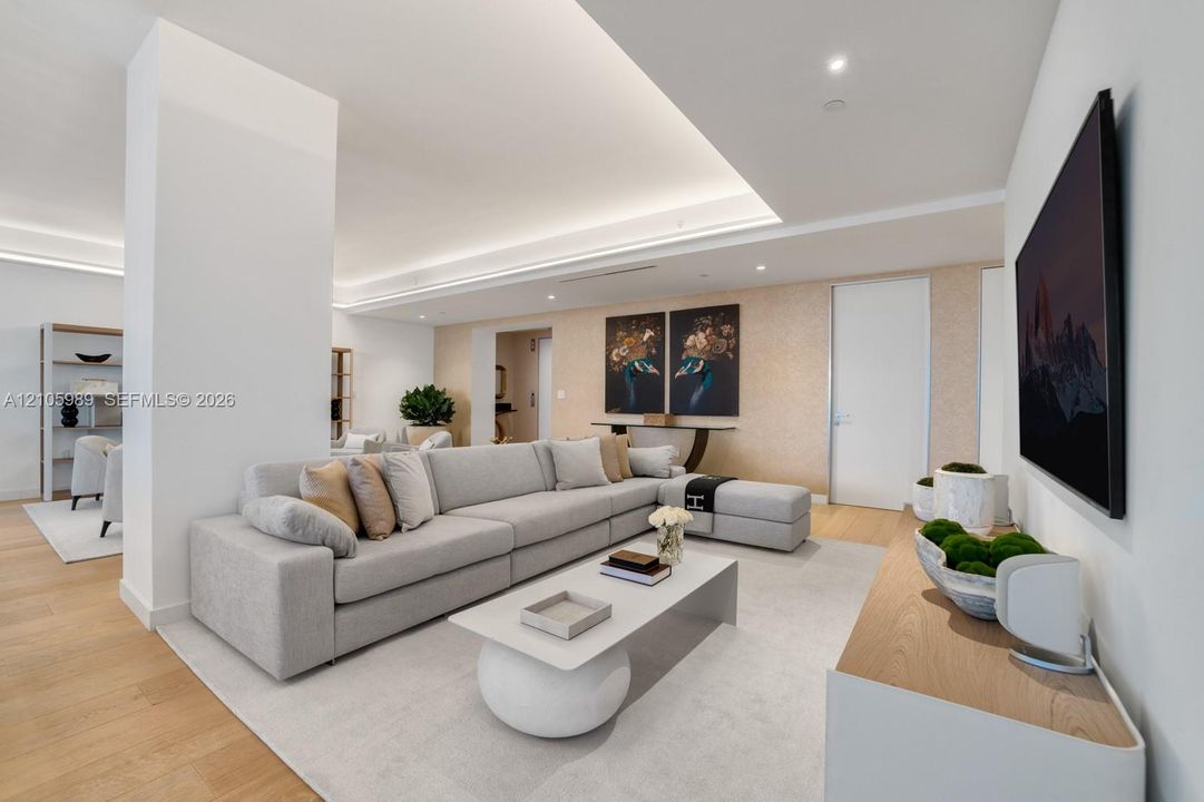 Recessed tray ceiling with integrated cove lighting, wood-finish flooring, and textured accent wall
