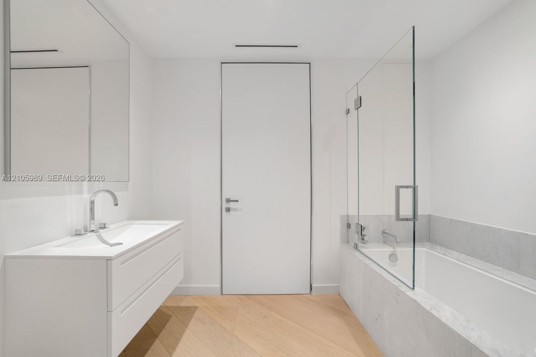 Wall-mounted floating vanity with integrated rectangular sink, wood-finish chevron flooring, frameless glass shower enclosure, and stone-surround soaking tub