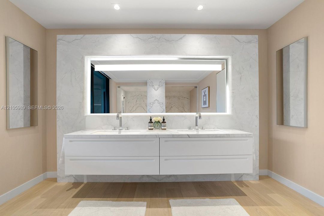Floating double vanity featuring a stone countertop, dual undermount sinks, full-width backlit mirror, and wood-finish flooring