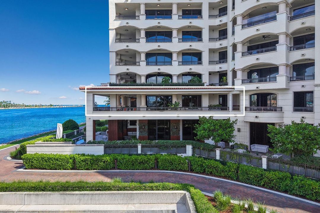 High-rise residence exterior featuring an expansive covered terrace with stone columns, metal railing, and direct water frontage