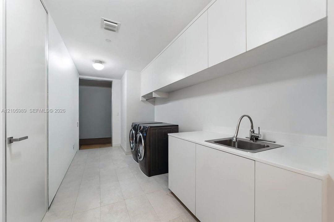 Utility space featuring expansive white cabinetry, white countertop, undermount stainless steel sink with a high-arch faucet, and large-format tile flooring