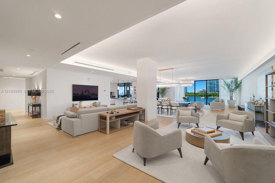 Open-concept living space featuring wood-finish flooring, recessed perimeter lighting, high ceilings, floor-to-ceiling windows, and water exterior